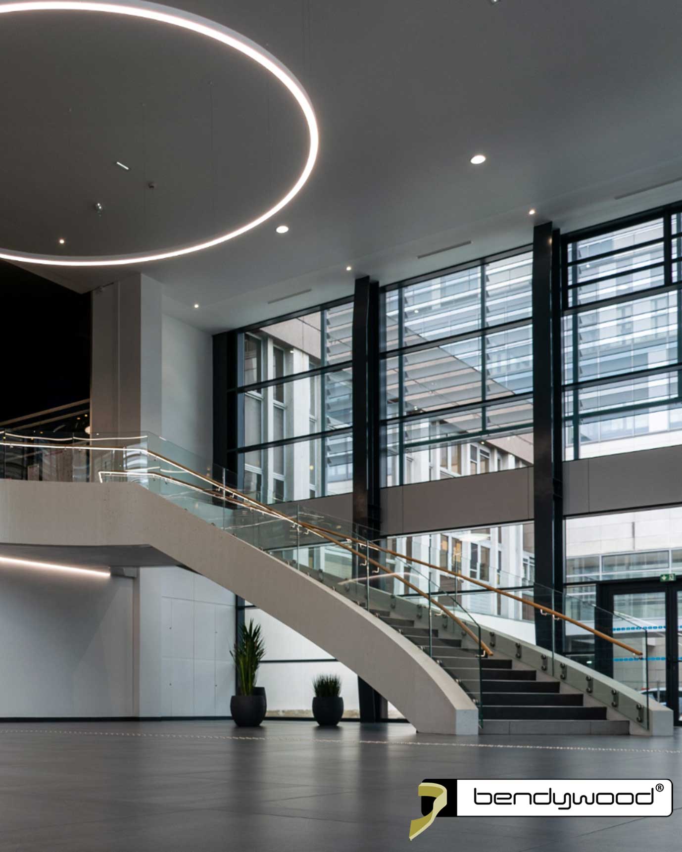 Scala curva con balaustra in vetro e corrimano in rovere Bendywood® con strisce LED. 